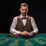 Portrait of a croupier is holding playing cards, gambling chips on table. Black background
